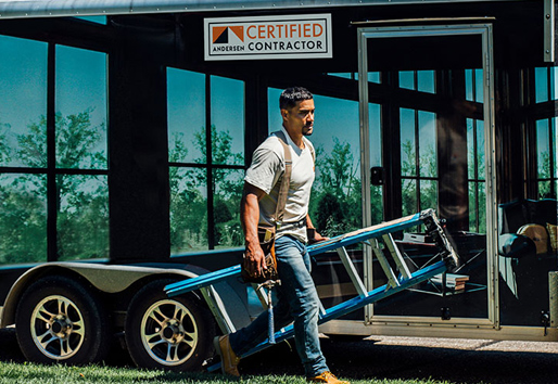 Certified Contractor carrying a ladder past his work trailer