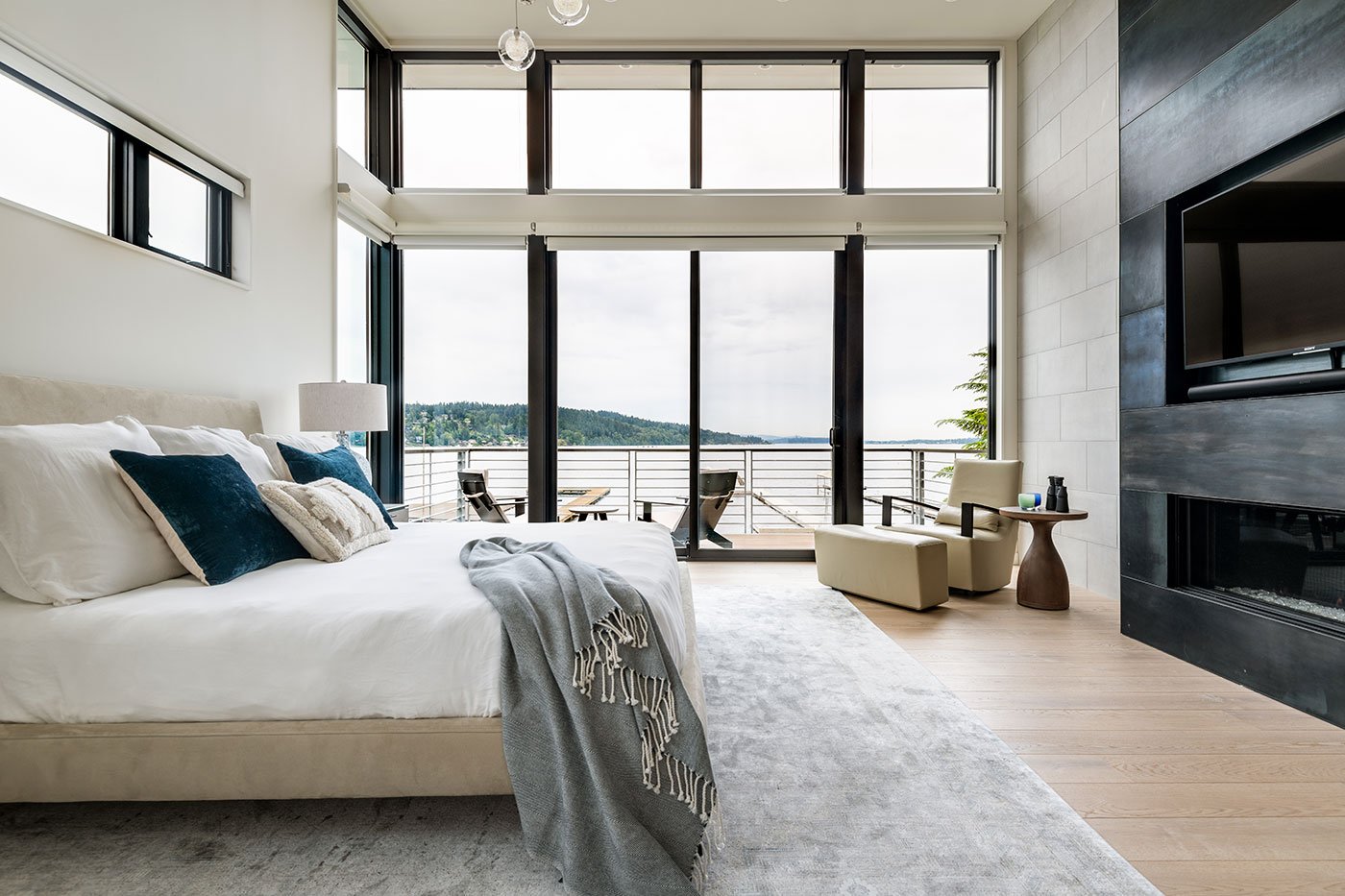 A bedroom with floor-to-ceiling glass showcasing lake views.