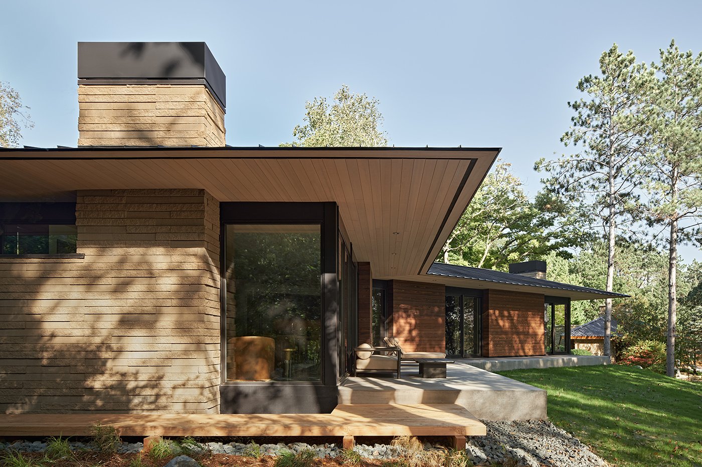 An exterior view of a single-story home with cedar siding, deep eaves, and lots of floor-to-ceiling glass.