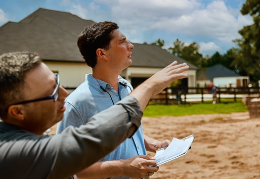 Two men stand on a building site discussing a project.