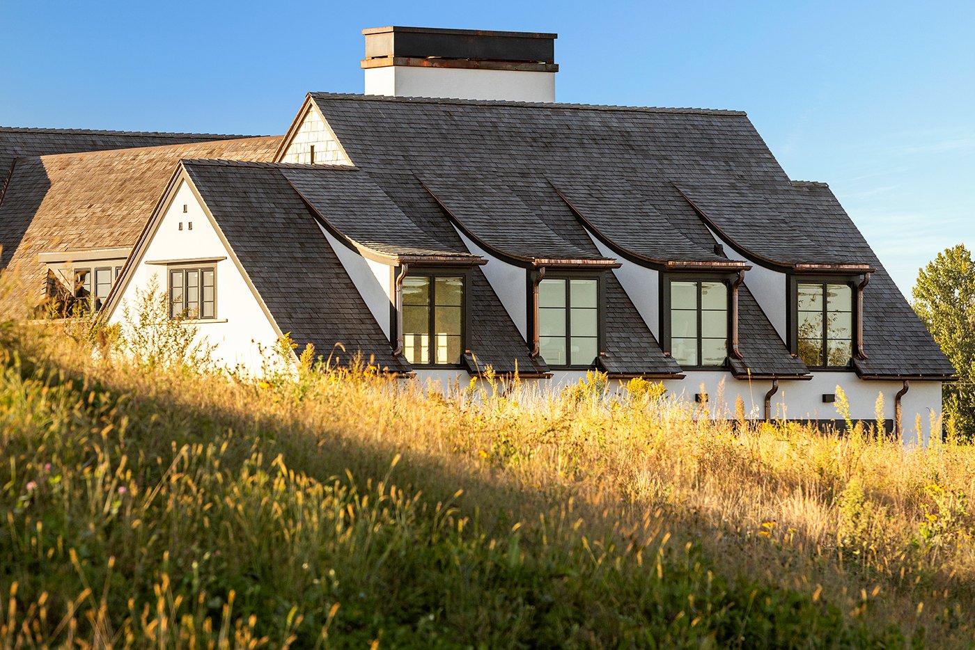 A roof punctuated by four dormer windows peeks over the brow of a hill covered in prairie grass at golden hour.