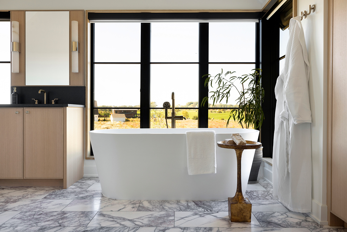 A bathroom with marble floors, floor-to-ceiling windows wrapping around a corner, and housing a soaking tub.