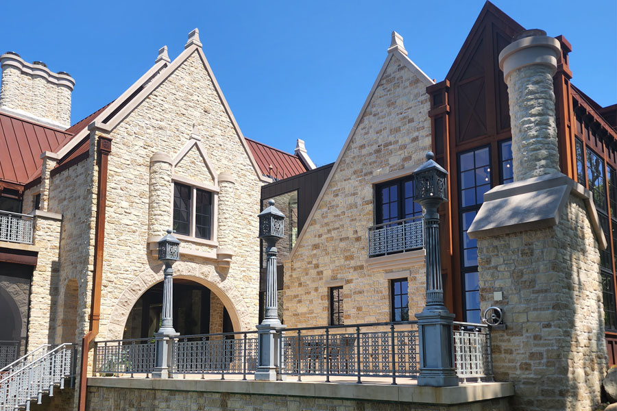 a stone building with gothic architectural features, including pointed arches, decorative columns and steeply pitched roofs. The building has multiple levels, large windows and a mix of stone and wood elements