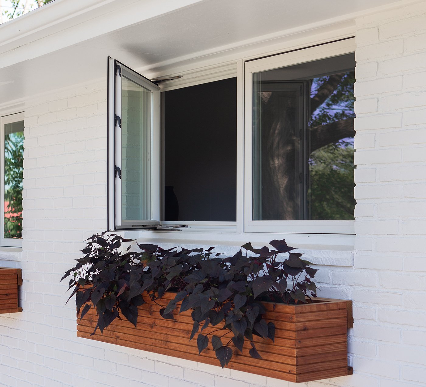 The exterior of a house with white brick siding and planter box underneath white 100 Series Casement Windows.