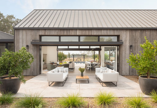 An exterior shot of a black Andersen®  MultiGlide™ Door that opens an entire wall to provide a seamless indoor/outdoor space between living room and courtyard.