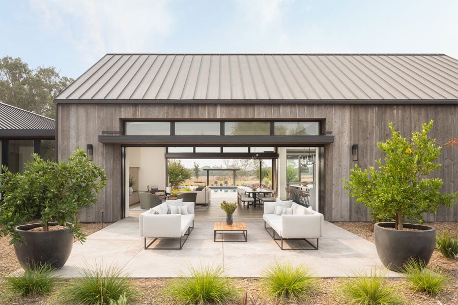 An exterior shot of a black Andersen®  MultiGlide™ Door that opens an entire wall to provide a seamless indoor/outdoor space between living room and courtyard.