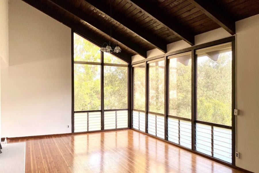 A living room with dark wood beamed ceilings and floor-to-ceiling windows that wrap around a corner.