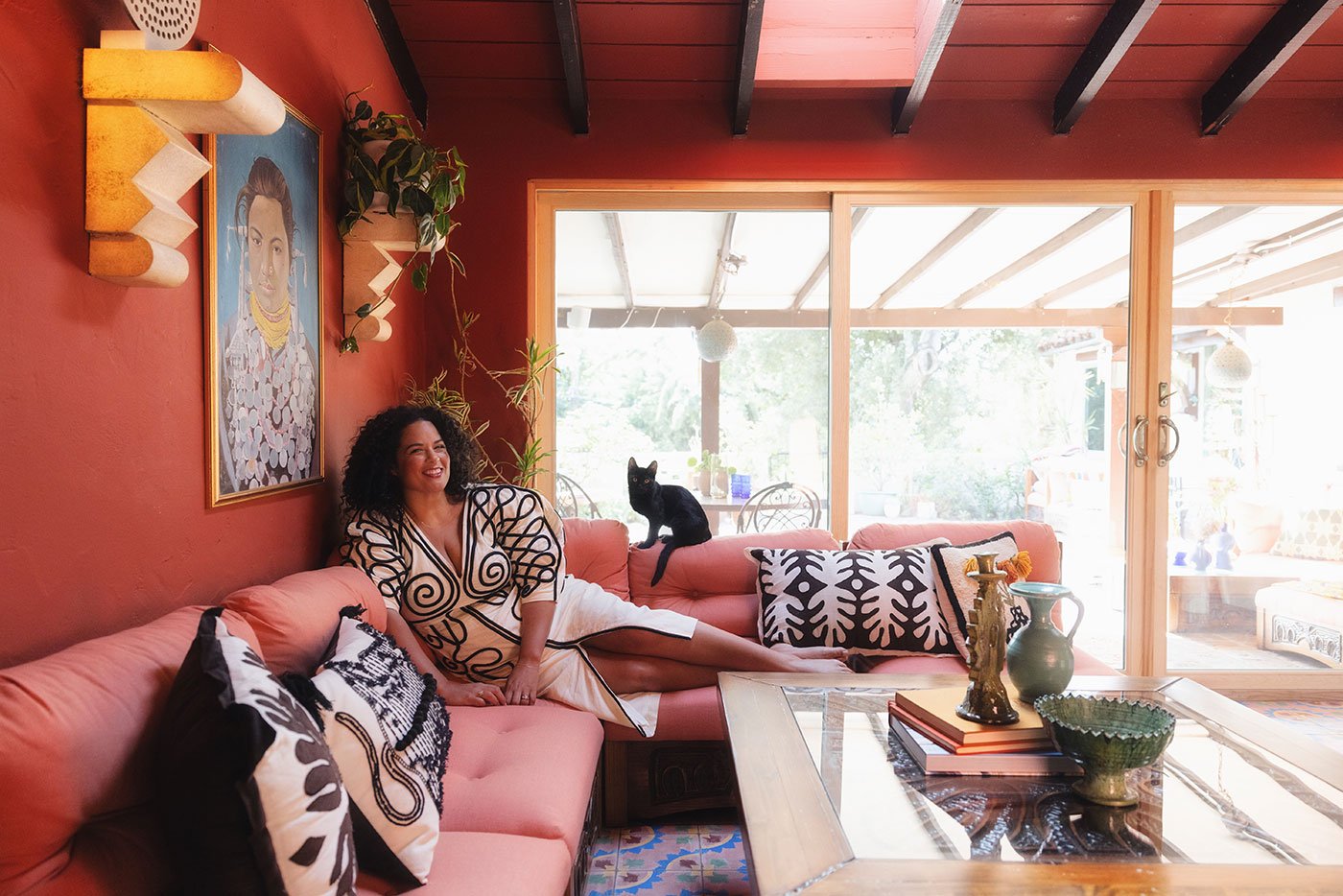 Justina Blakeney and her cat lounge on a rose-colored couch on her lanai which connects to the courtyard outside via an E-Series Gliding Patio Door.