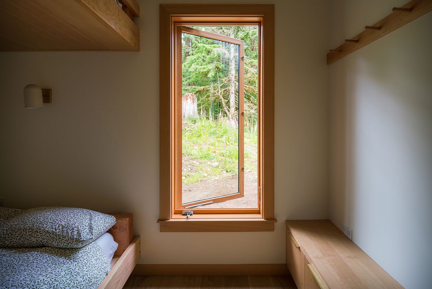 A bunkroom with an open casement window and row of built-in storage and hooks.