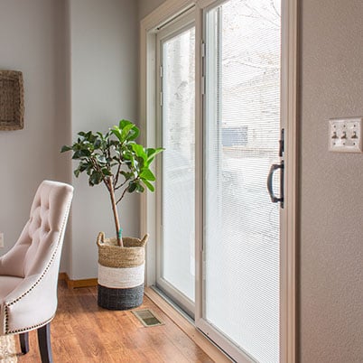 Andersen 200 Series blinds in glass white framed sliding patio door with chair and plant