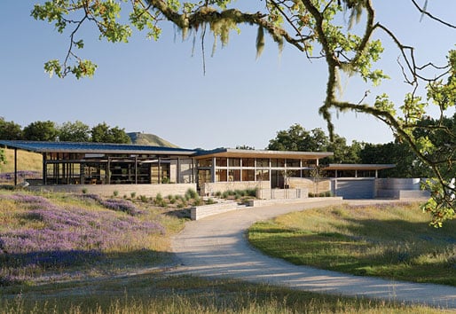 A view down a curved driveway of the home, which is characterized by a long, low-slung profile.