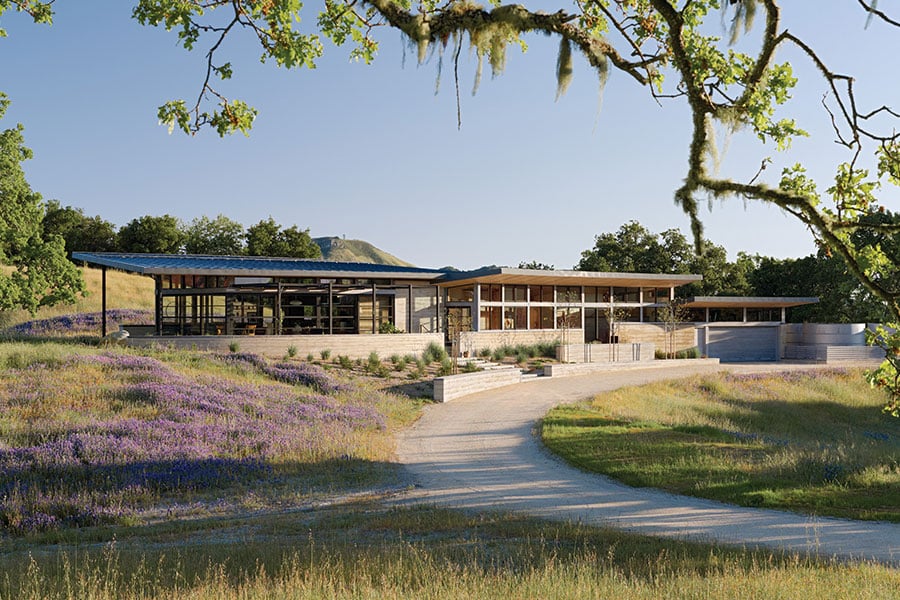 A view down a curved driveway of the home, which is characterized by a long, low-slung profile.