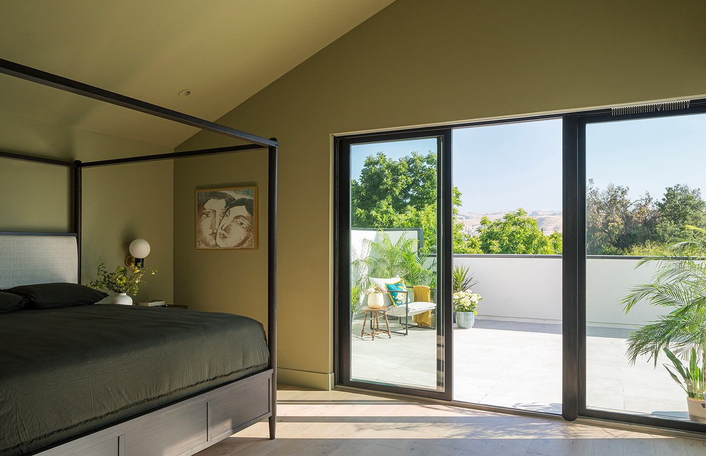 A green bedroom with a black 100 Series Gliding Patio Door leading to a large balcony.