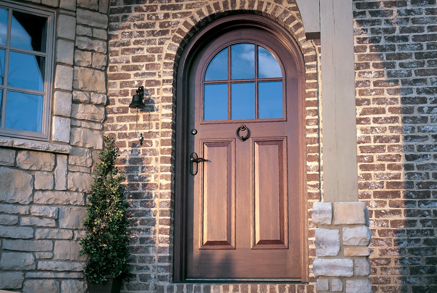 A dark wood arched front door with upper glass panels surrounded by brick. 