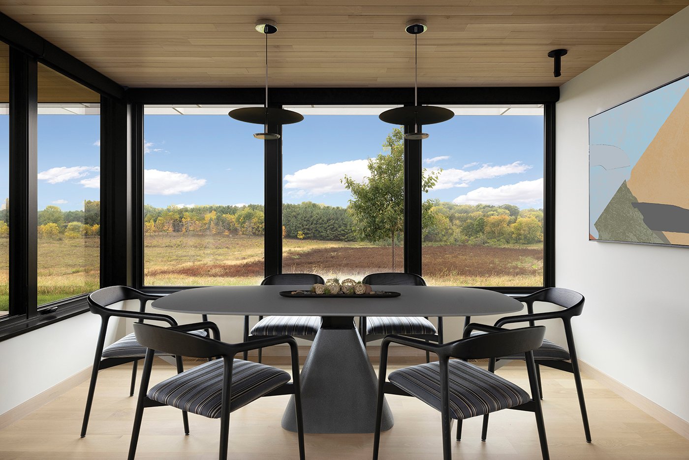 A dining table surrounded by two walls of Andersen® E-Series Casement Windows with black frames showcasing a prairie view.