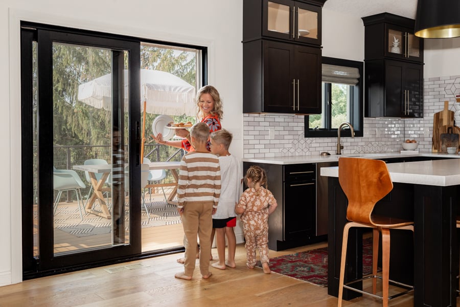 A family smiling in a kitchen next to a black sliding glass patio door. 