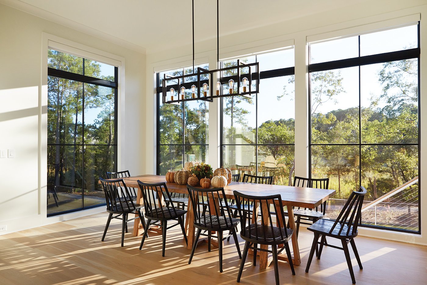 A dining room table decorated with pumpkins, surrounded by floor-to-ceiling windows with black frames.