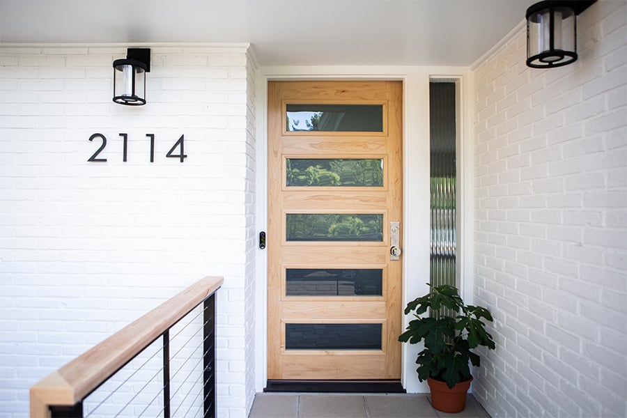 A natural wood front door with five horizontal windows and a sidelight next to it completes the clean, modern look of a white-painted brick home.