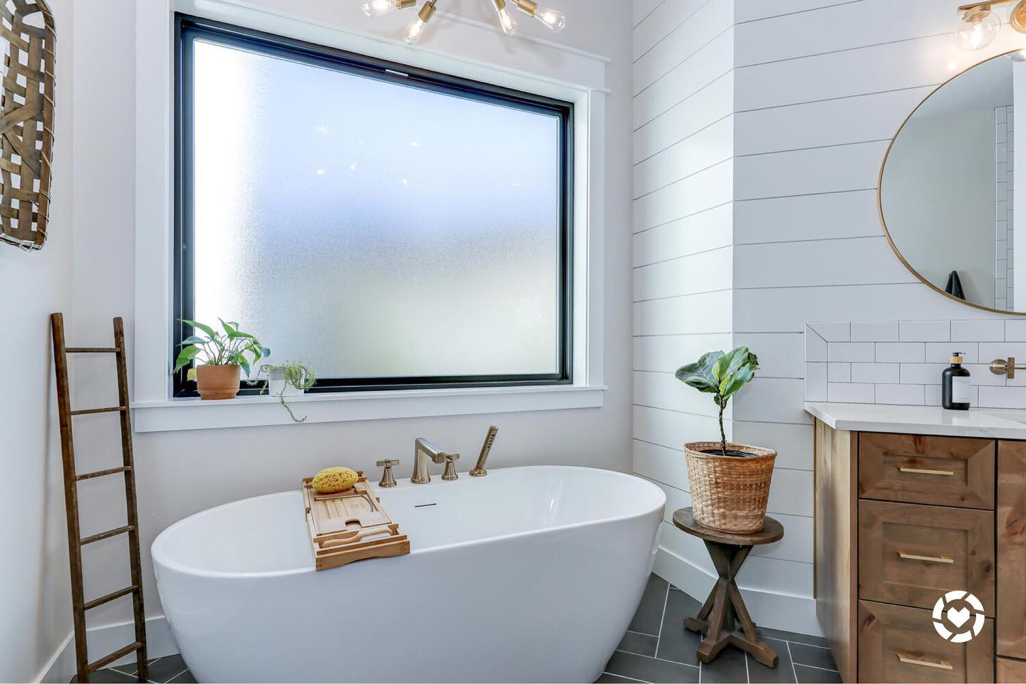 A soaking tub underneath a large rectangular picture window with obscure glass in a bathroom with white walls and a black tile floor.