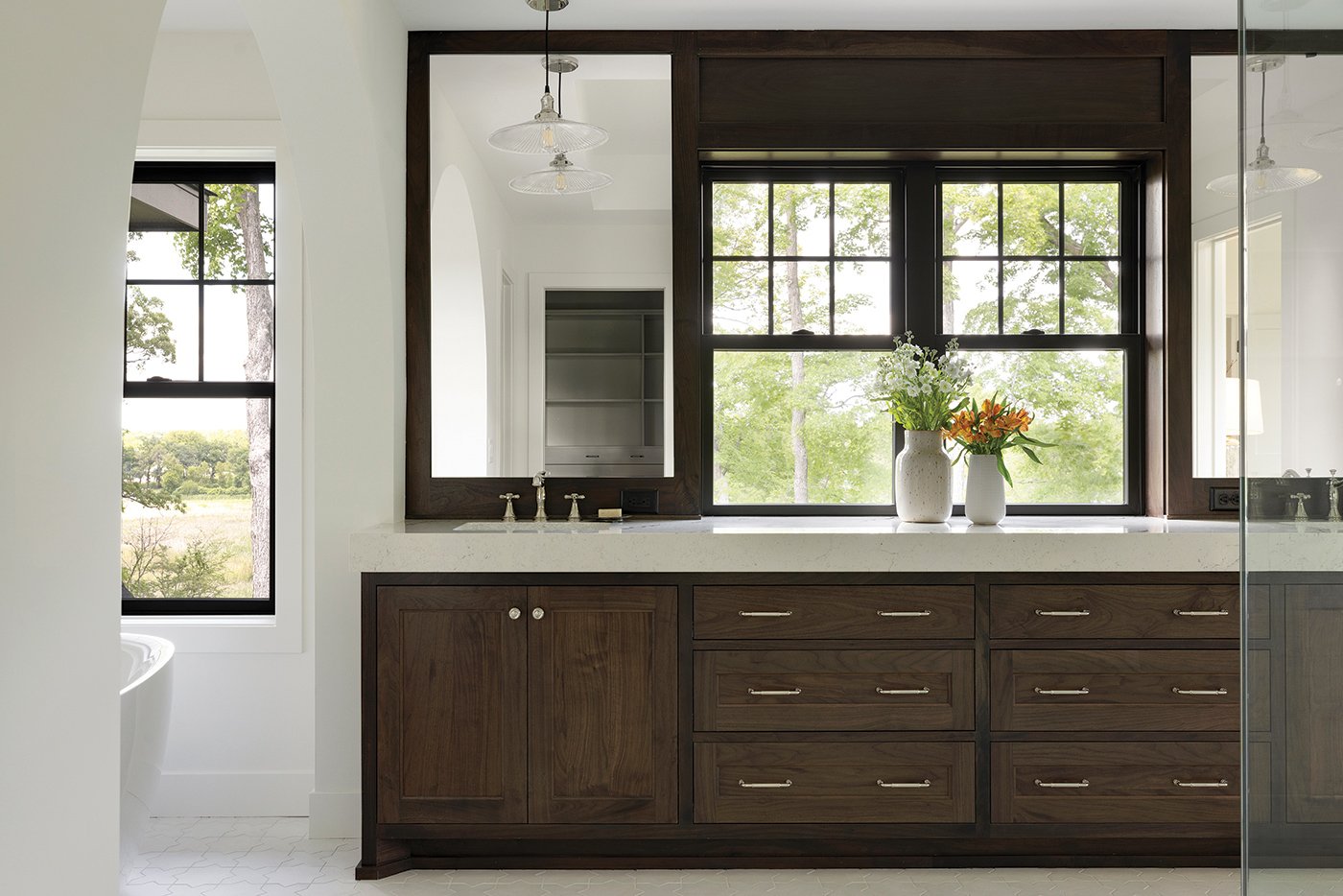 A bathroom with a pair of single-hung windows in between the sinks and mirrors.