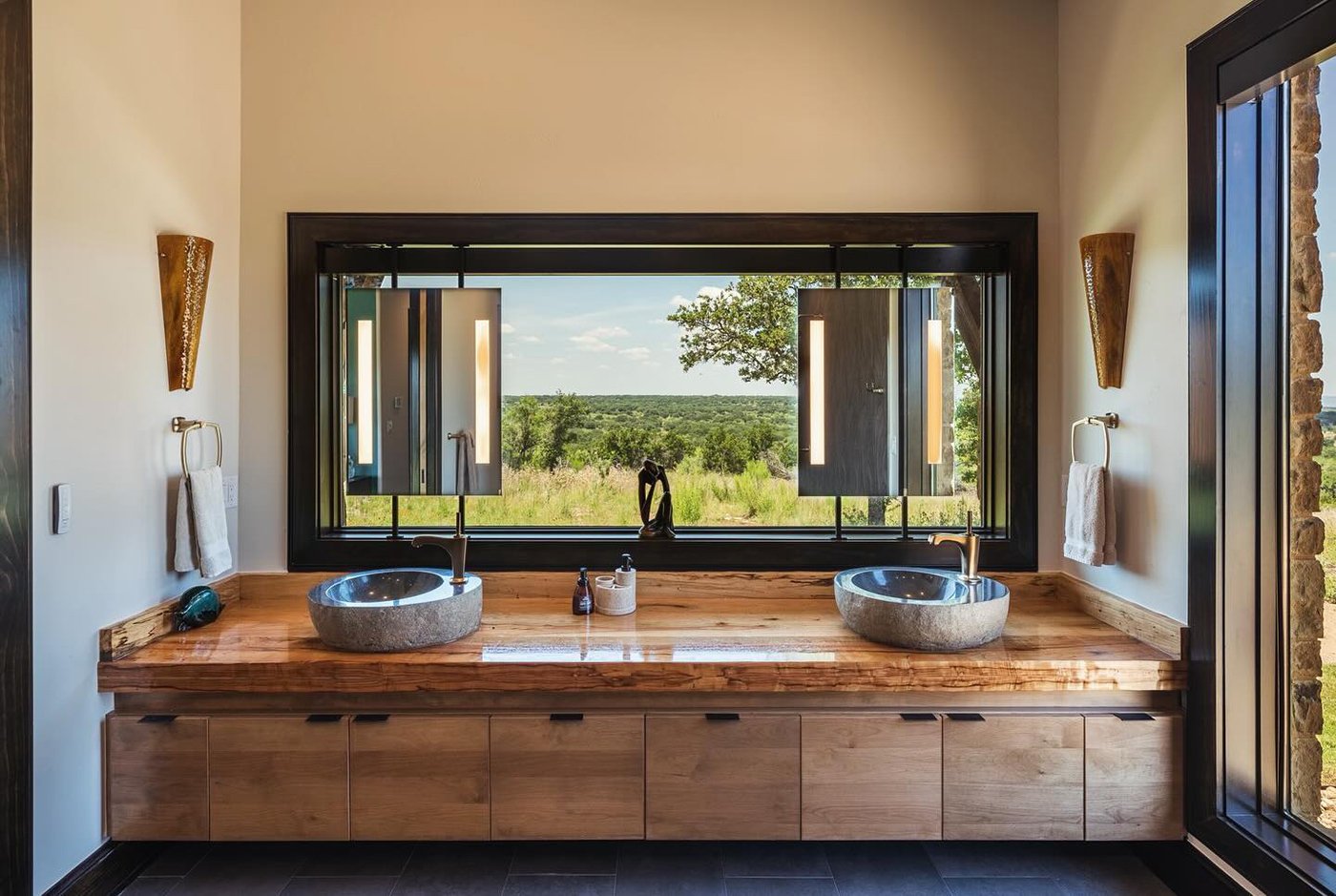 A bathroom with a large horizontal picture window over the bathroom sink and mirrors hanging over the window.
