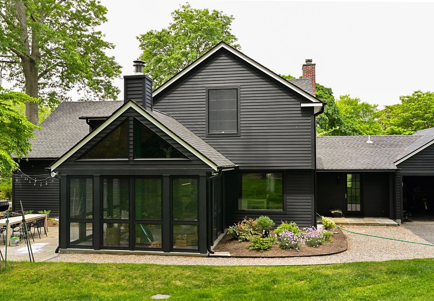 An exterior shot of a black, two-story Cape Cod home with a porch and patio.
