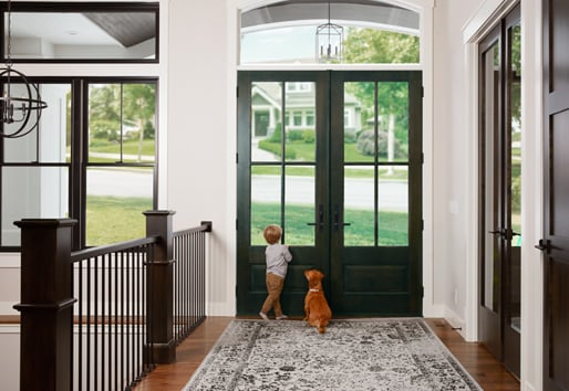 A boy and his dog wait at a double front door.