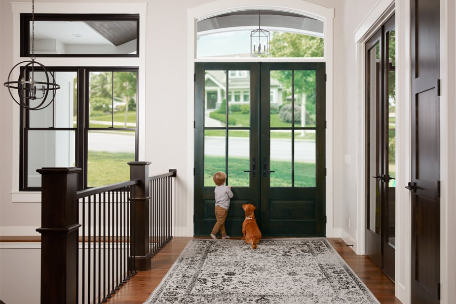 A boy and his dog wait at a double front door.