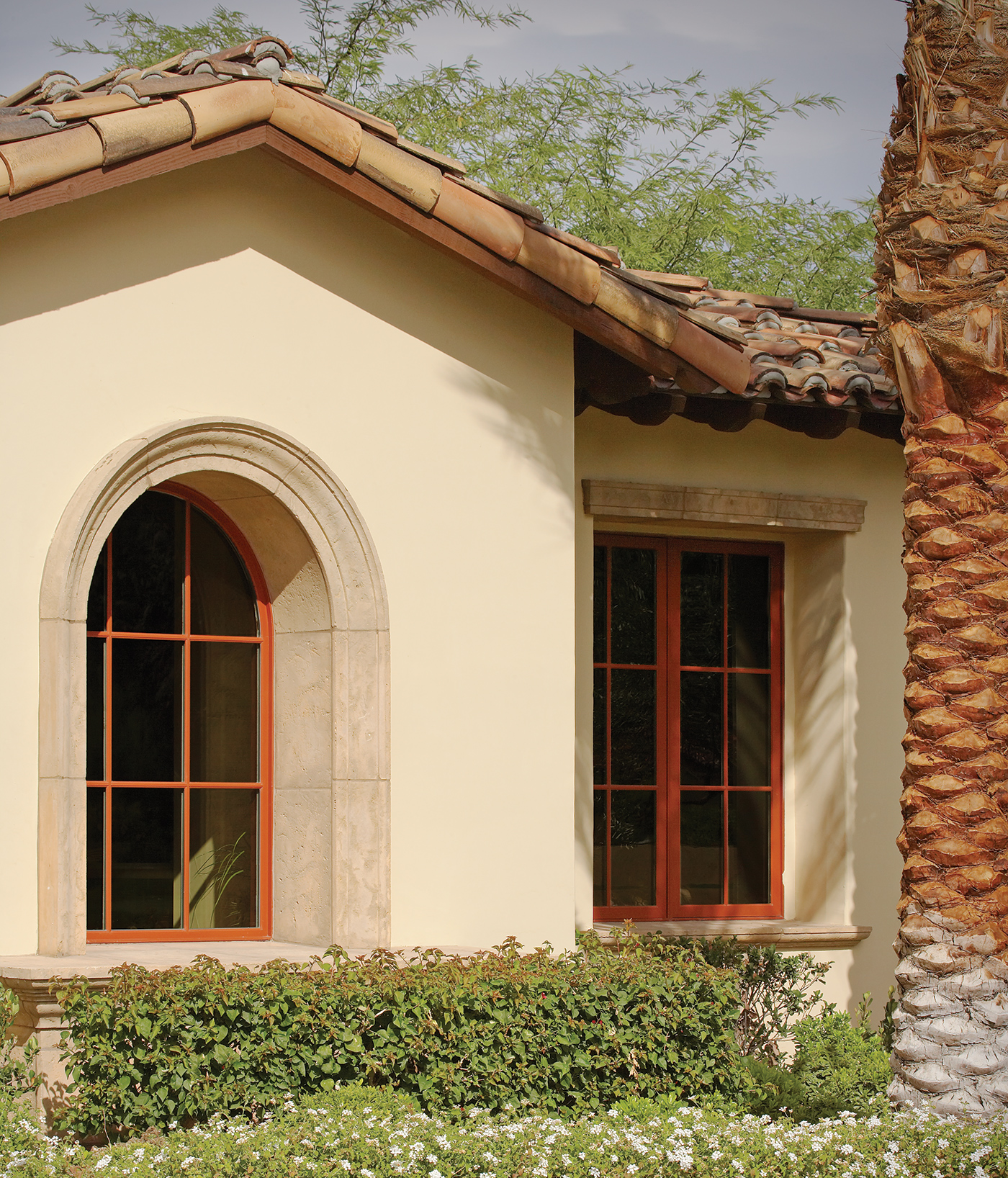 A Spanish-style stucco home with a tile roof and an arched specialty window with a burnt orange exterior and colonial grilles. 