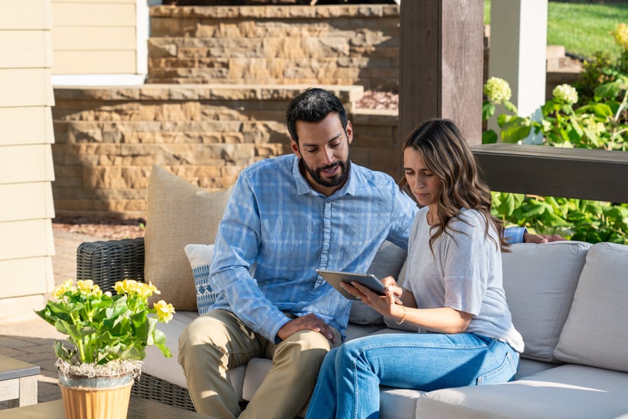 A couple seated on a patio look at a tablet together.