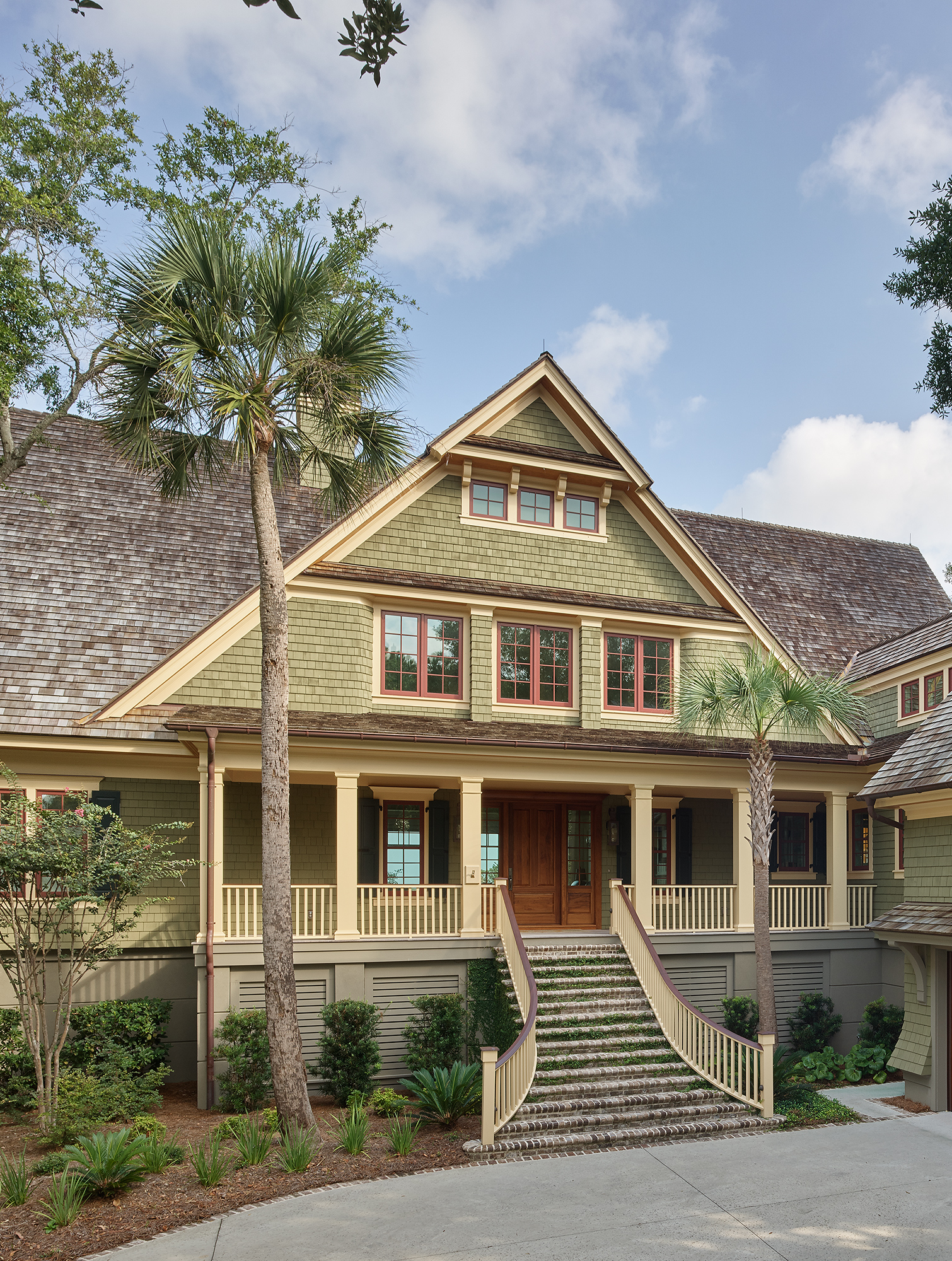 A multiple-story house with green shingle siding and steeply pitched gray shingle roof, with colonial grille patterns on the windows.