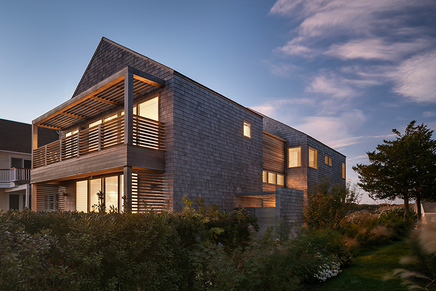 A two-story house with porches on each level and cedar shingles at dusk. 