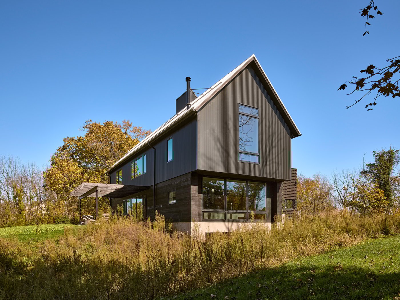 A black house with steep pitched roof and picture windows during the day. 