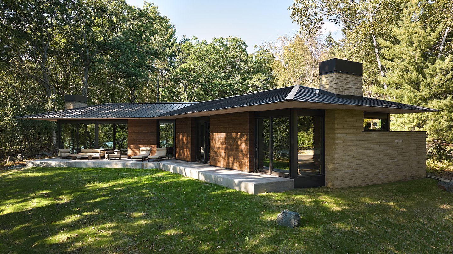 An exterior shot of a home influenced by Frank Lloyd Wright with a single-story layout, prominent roof, and lots of floor-to-ceiling glass.