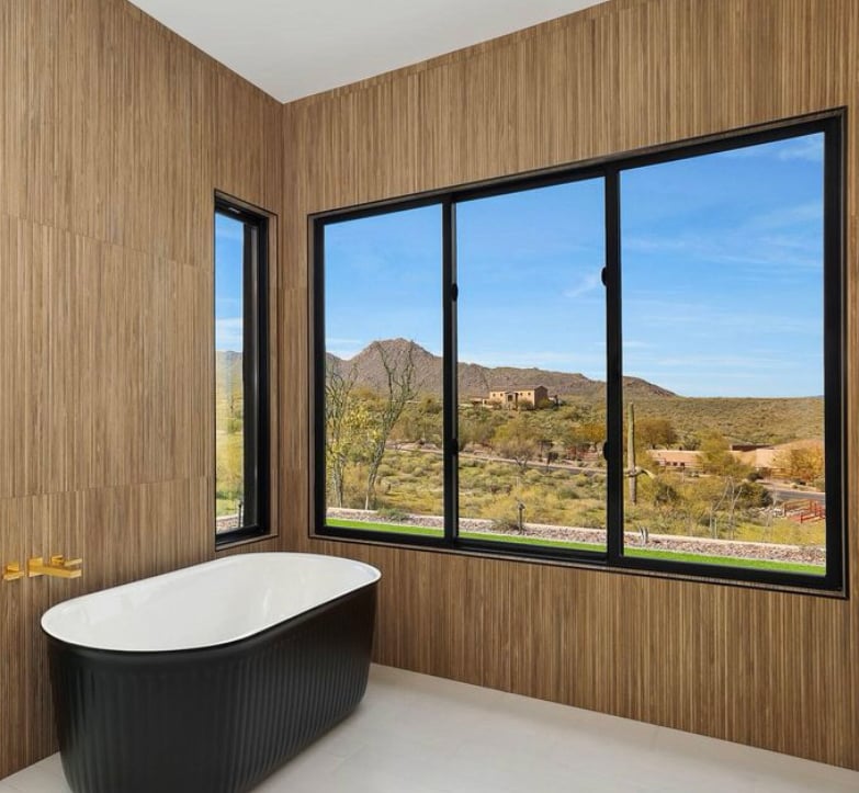 Close-up interior bathroom rendering of a contemporary luxury home in the desert with a wall of large, black Andersen® 100 Series Picture Windows providing unobstructed views of the landscape beyond.