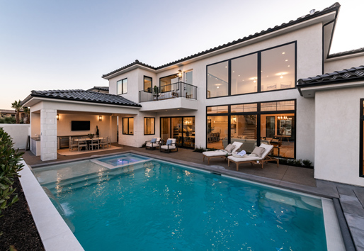 An outdoor dining area next to an underground pool with large, black windows and doors allowing deck access