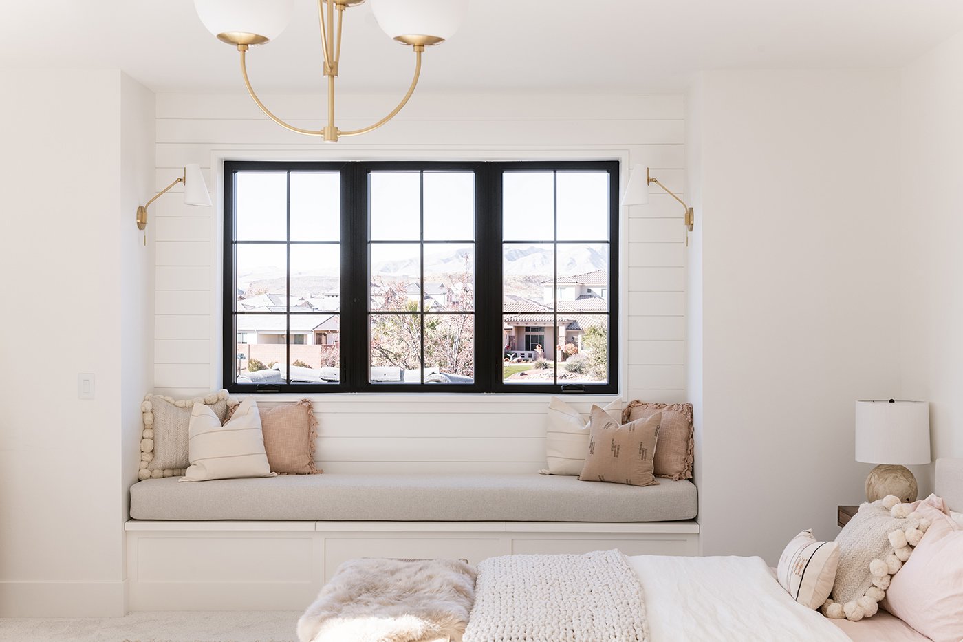 Close-up of a large window unit made of three windows with black frames and window grilles that pop against a white wall and coastal neutrals.