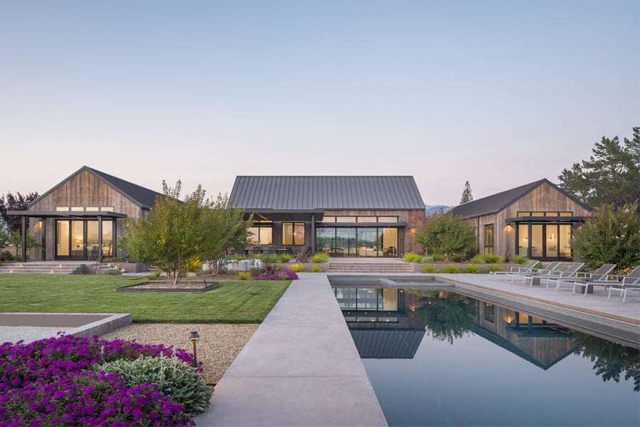 A farmhouse with hills in the distance and E-Series windows and doors leads into a backyard with a pool. 