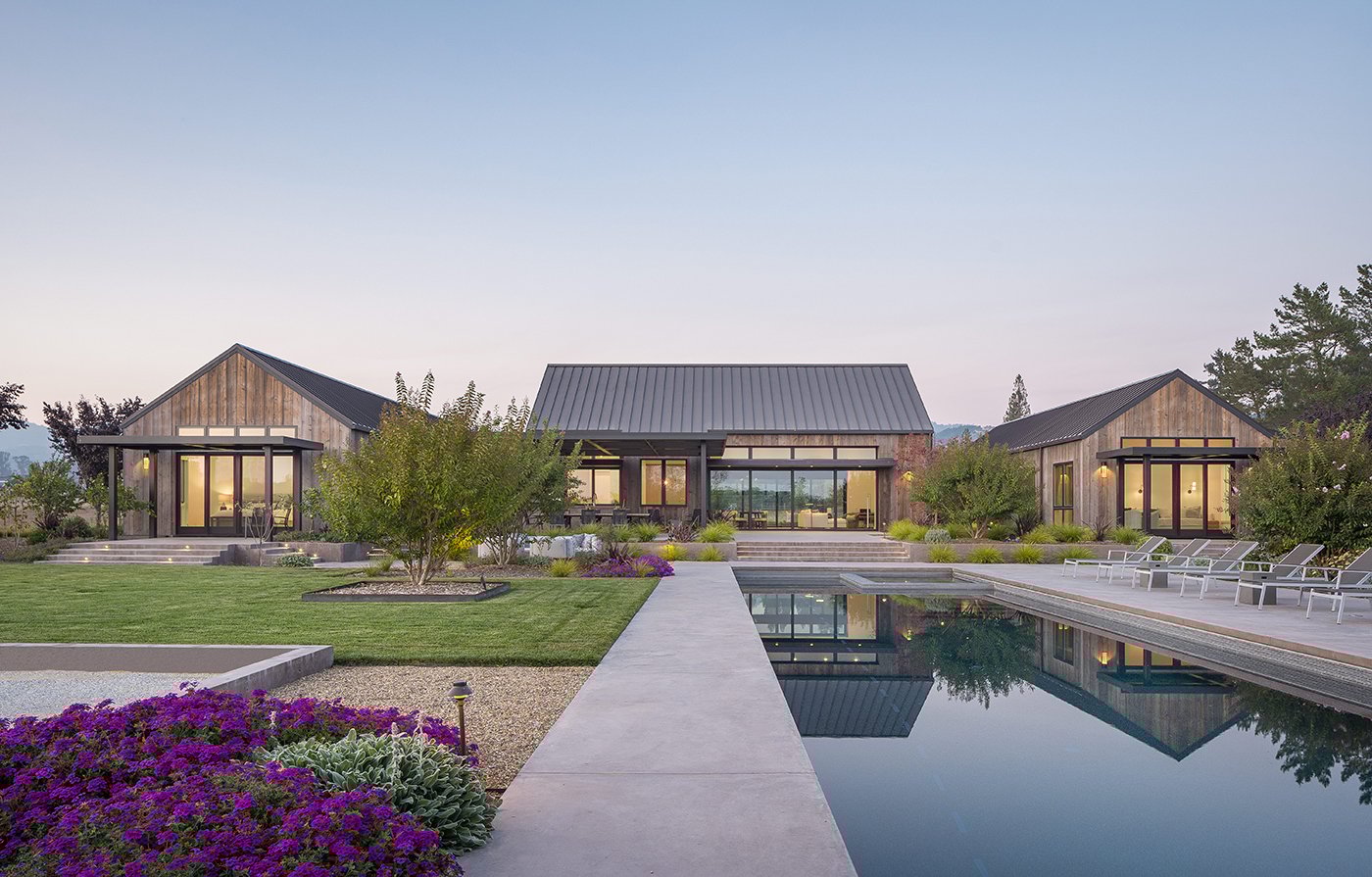A farmhouse with hills in the distance and E-Series windows and doors leads into a backyard with a pool. 