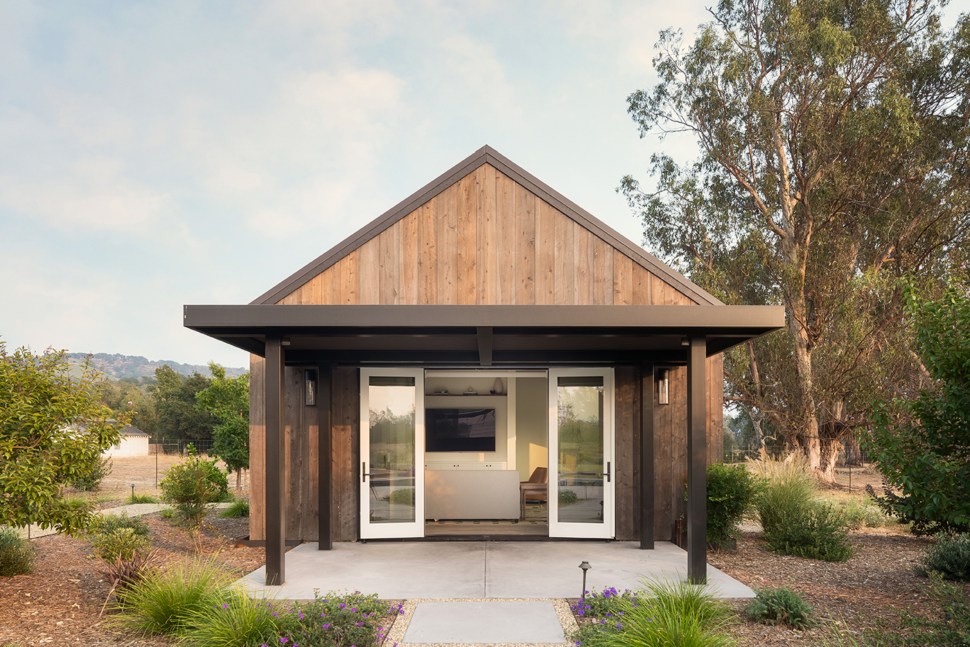An exterior shot of a pool house with wood paneling, an overhang, and Andersen E-series four panel hinged patio door. 