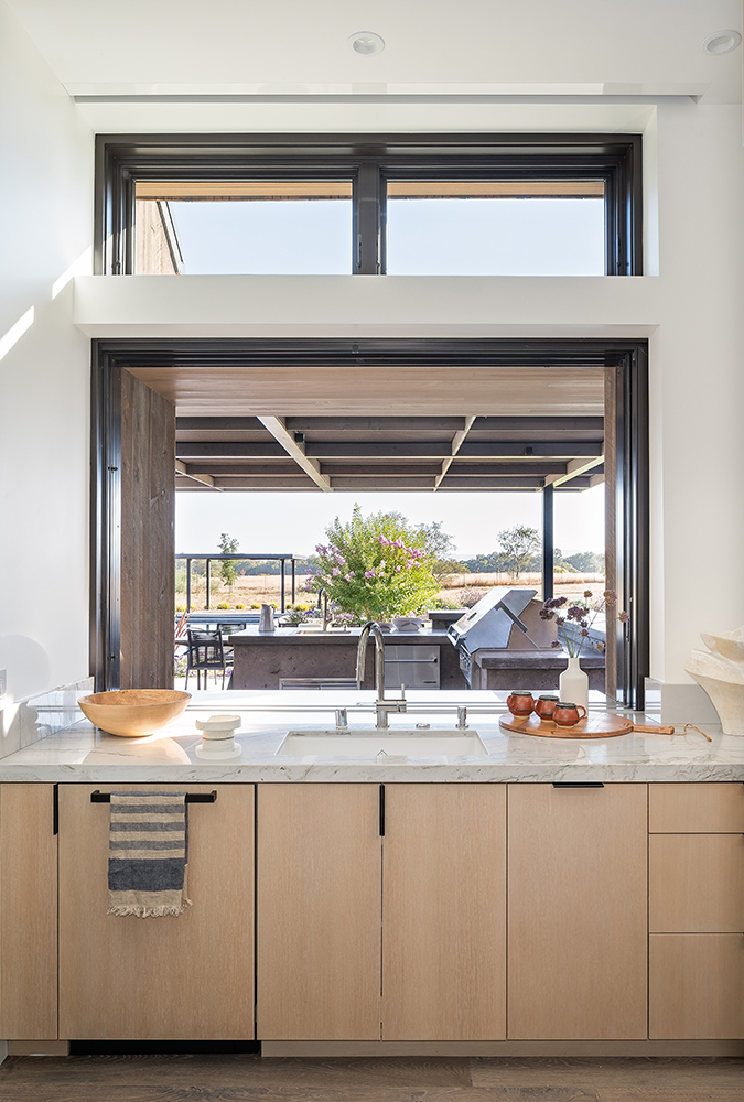An interior shot of a kitchen sink in front of a pass-through window leading into an outdoor kitchen. 
