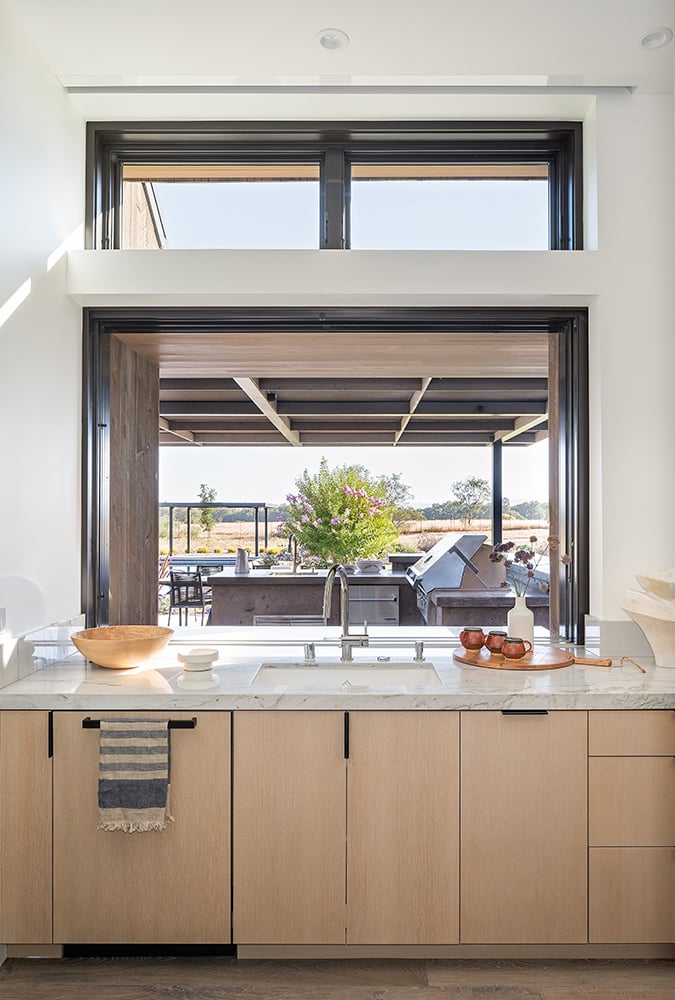 An interior shot of a kitchen sink in front of a pass-through window leading into an outdoor kitchen. 