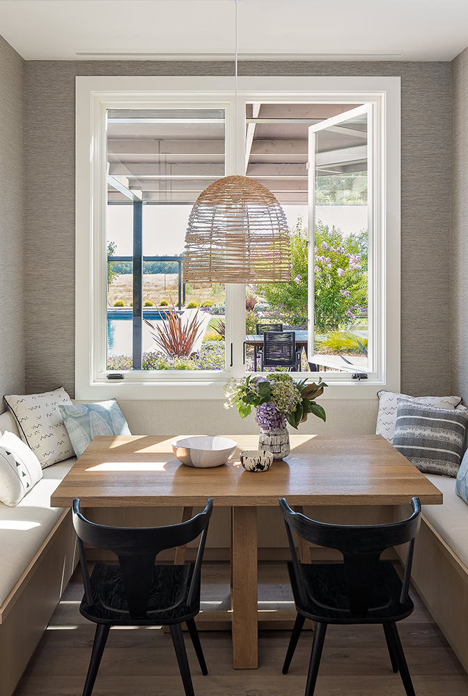 A nook with a wooden table and couch under two E-Series casement windows.