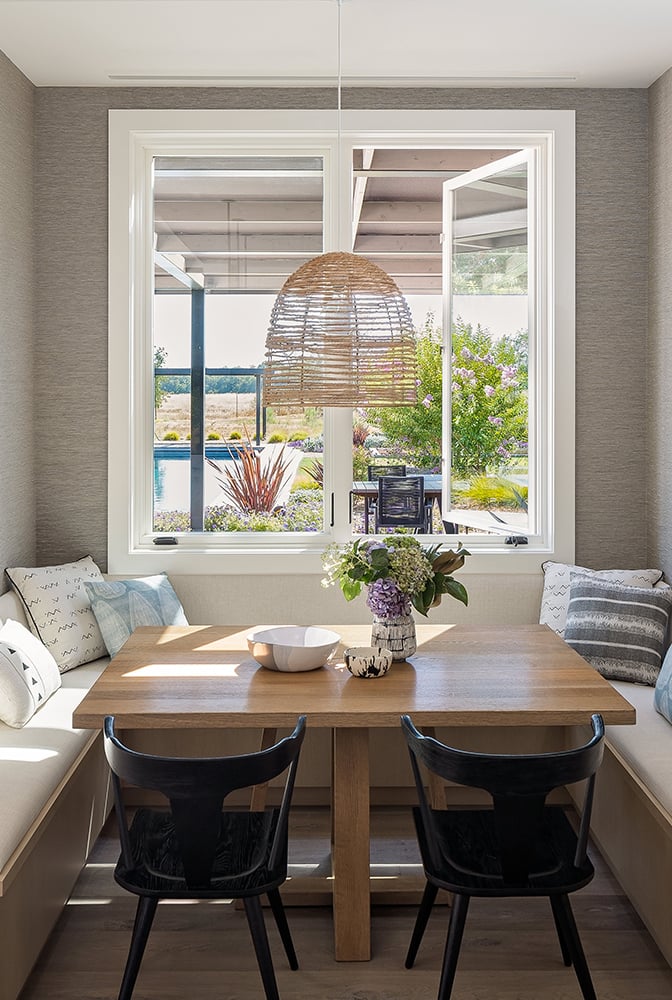 A nook with a wooden table and couch under two E-Series casement windows.