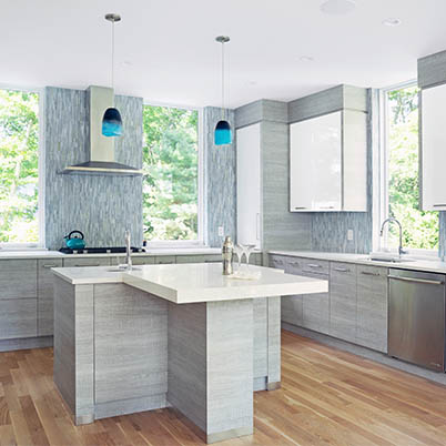 Interior of modern grey kitchen with wood flooring, white counters, blue light fixtures, and Andersen Windows.