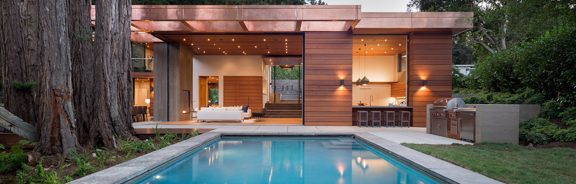 A modern home surrounded by nature and a 14-foot-tall Andersen® Liftslide Door that opens up the entire front-facing wall to the outdoor landscape and pool.