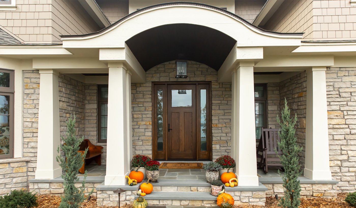 A dark stained wood front door with upper glass panel and sidelights complimenting a Craftsman home with a lightly colored, neutral stone exterior.
