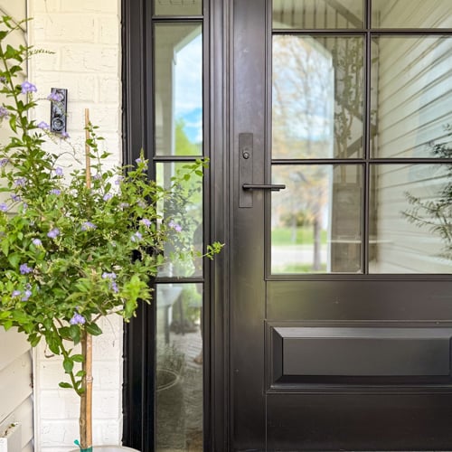 A modern front door with a light-colored wood exterior and horizontal glass panels popping against the white brick walls of a Mid-Century Modern home.