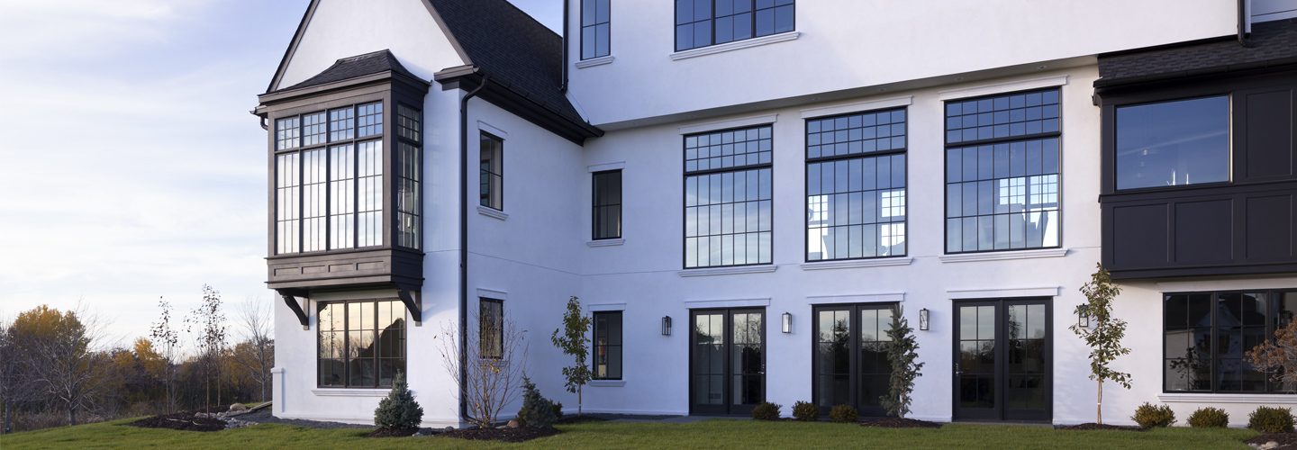 A modern Tudor with a white exterior and black Andersen® windows, including an oversized bay window.