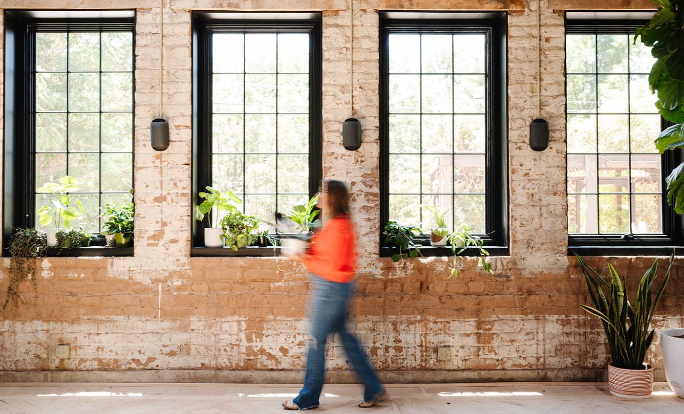 An exposed brick wall punctuated by four Andersen® A-Series Casement Windows with black frames and a 3-over-5 colonial grille pattern.